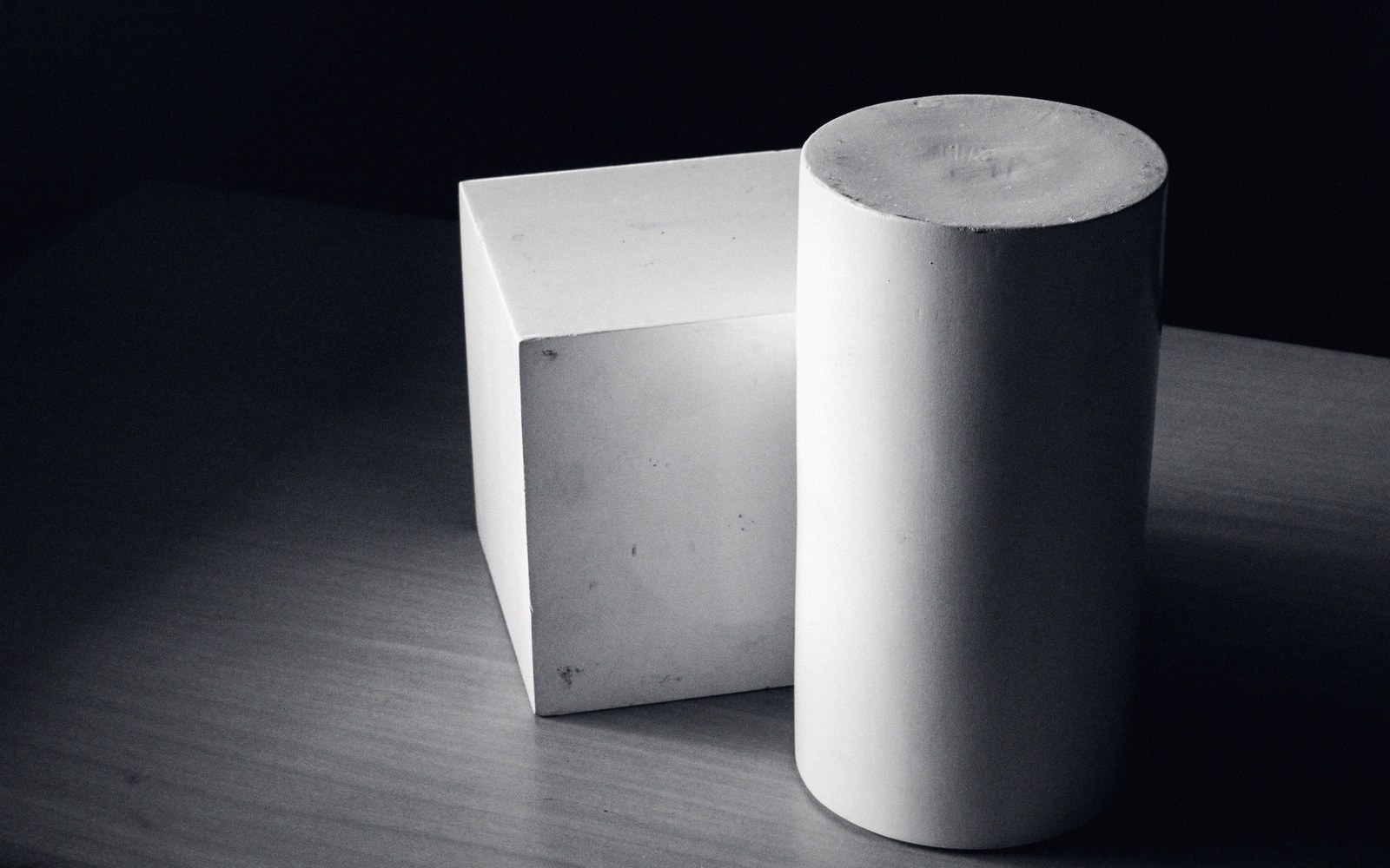 White cube and cylinder plaster shapes resting on a wooden surface