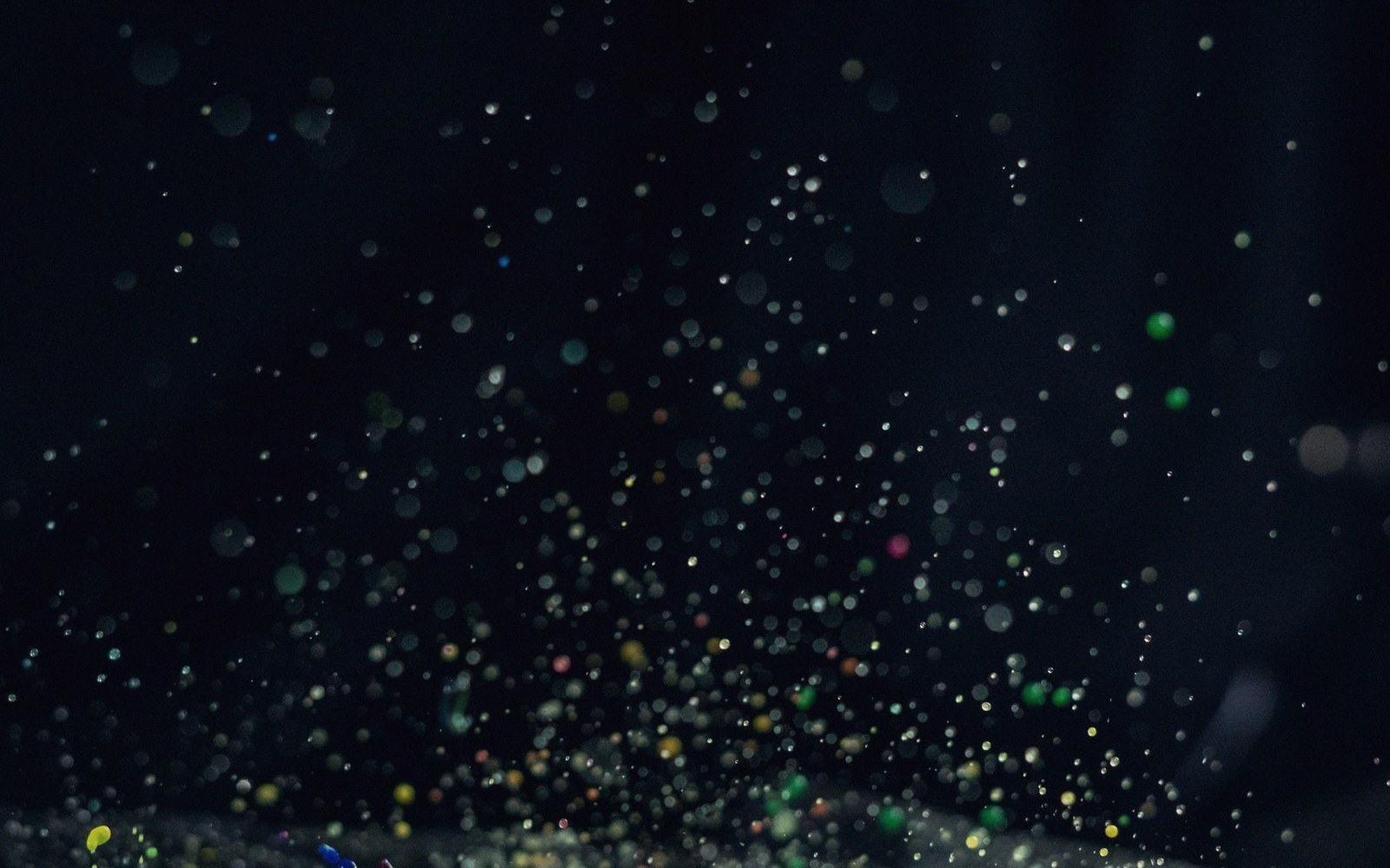 Scattered colorful bokeh lights float against a dark background like glowing particles