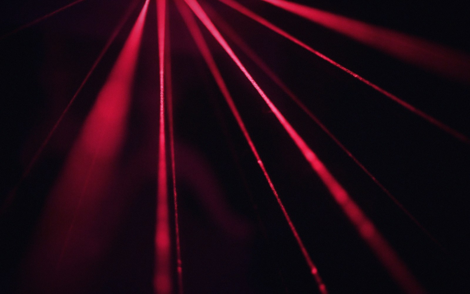 Multiple thin red laser beams fan out diagonally against a dark background