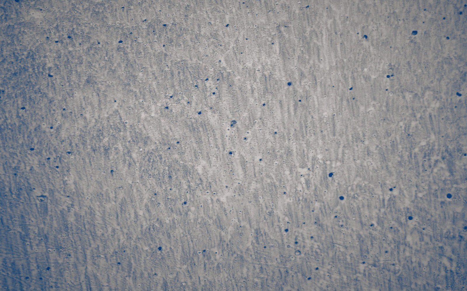 Close-up of a textured gray surface speckled with small dark spots and fine scratches