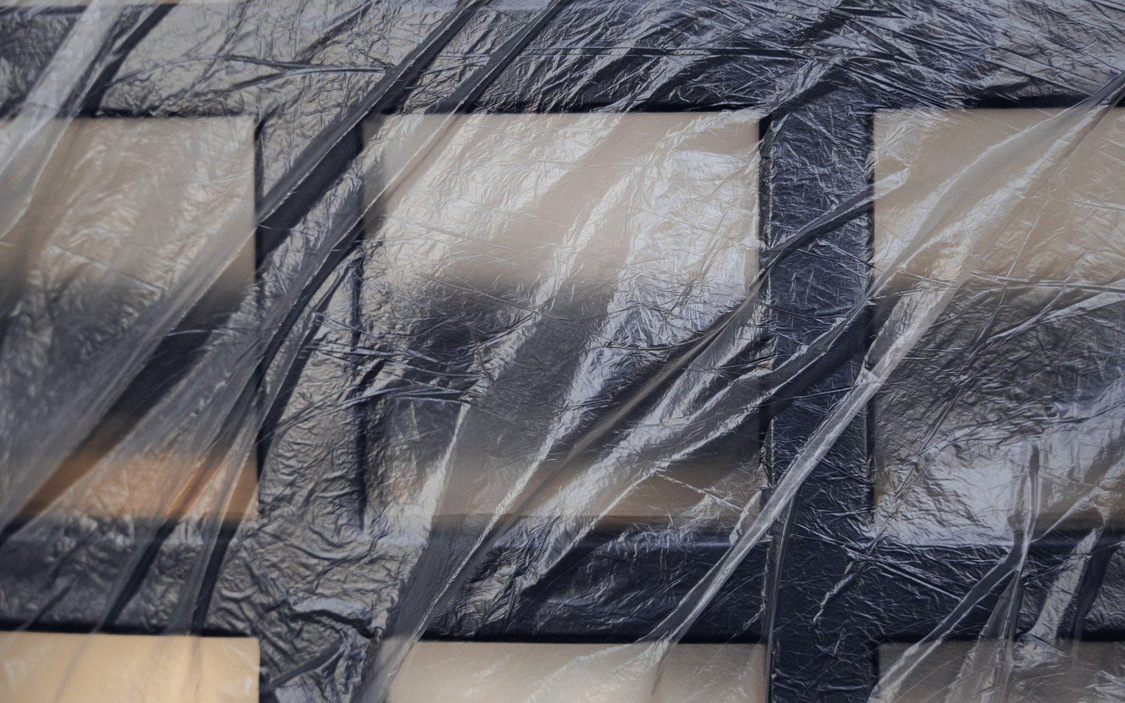 Wrinkled plastic sheeting stretched over a dark tiled surface with light and shadow patterns