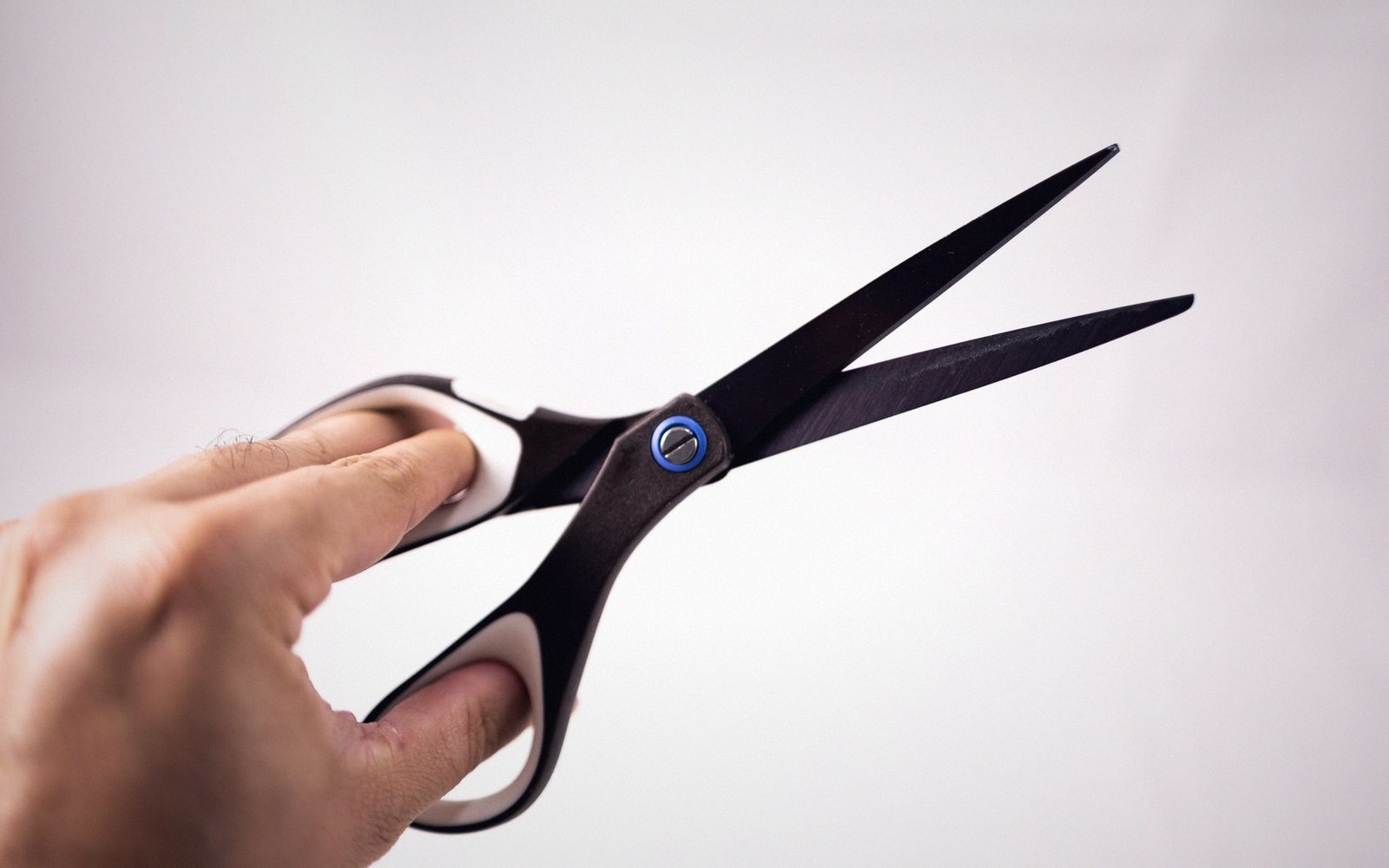 A hand holds open a pair of black-bladed scissors against a plain background