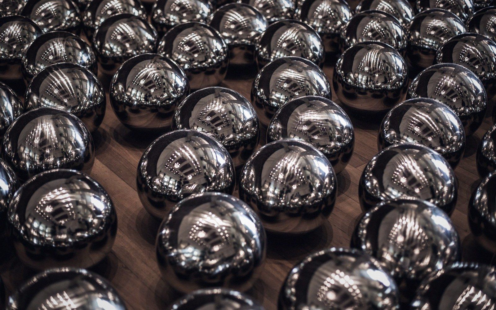 Rows of reflective mirrored spheres arranged closely together on a wooden floor